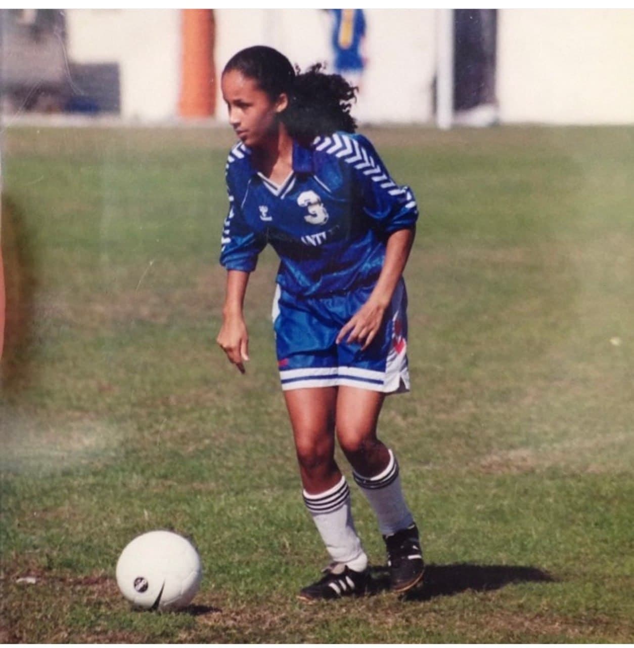 Christine Sylvain playing soccer in a blue jersey on a grass field