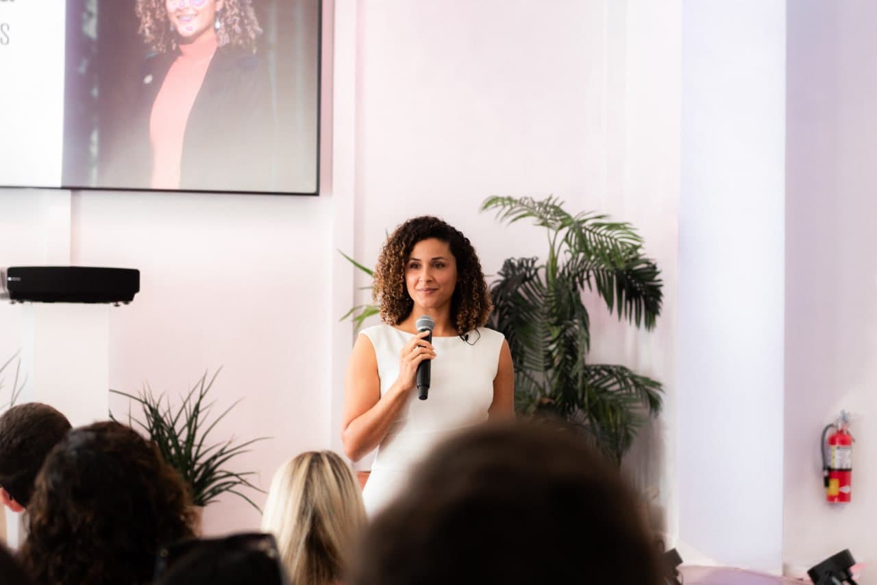 Christine Sylvain speaking with glamour portrait on screen behind her